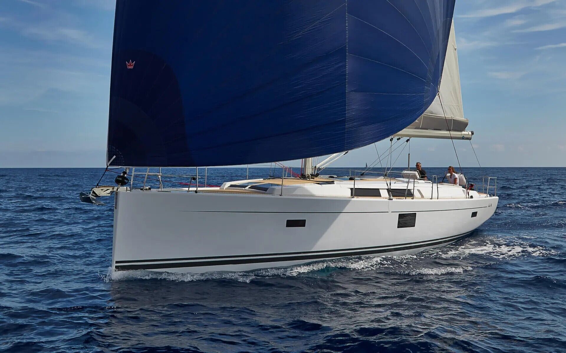 Un velero con casco blanco y vela azul navegando en el océano.