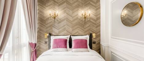 Habitación de hotel con cama, dos apliques, un espejo redondo y un papel tapiz con estampado en zigzag.