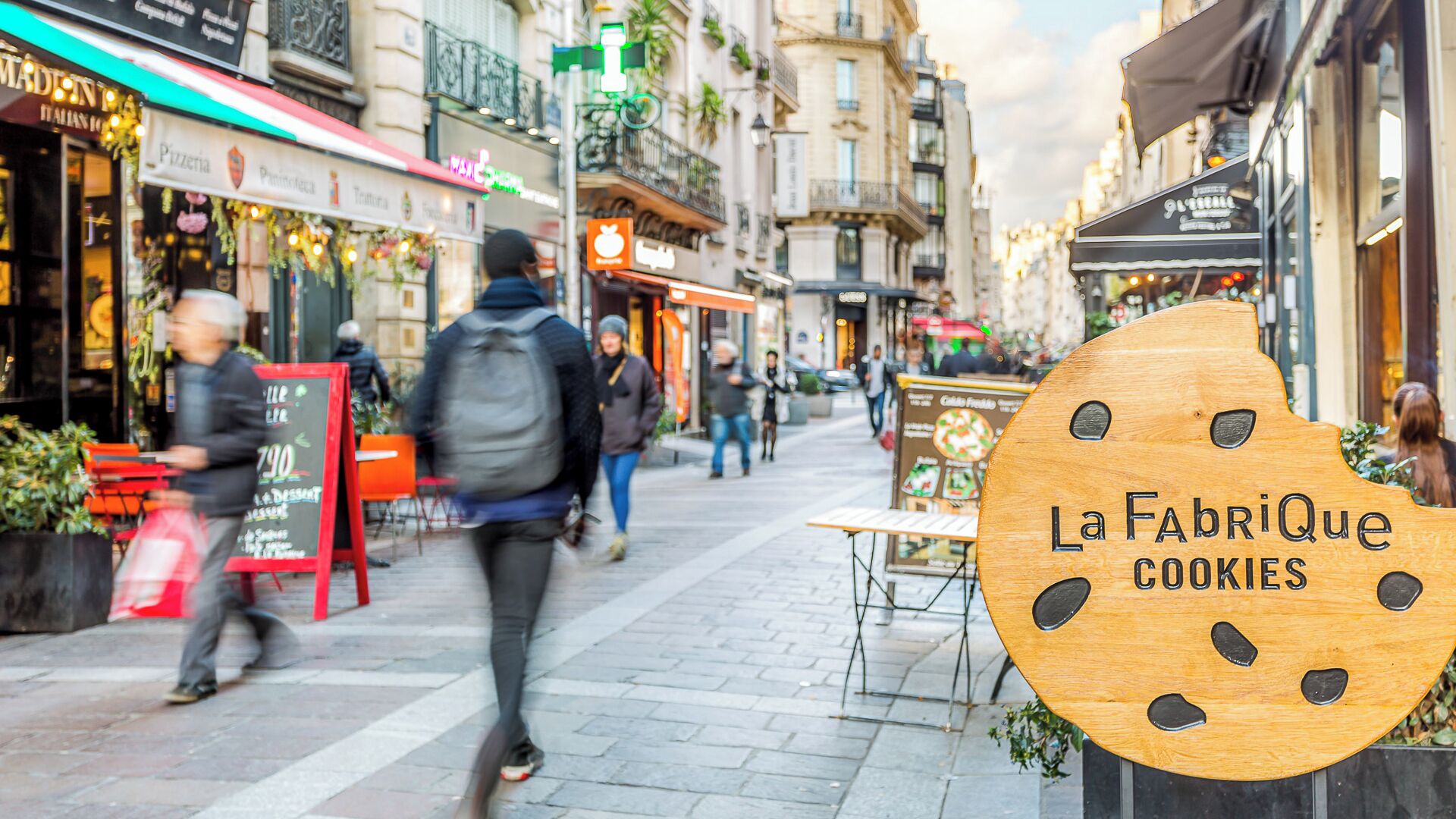 A street with shops and a sign for 'La FabriQue Cookies'.
