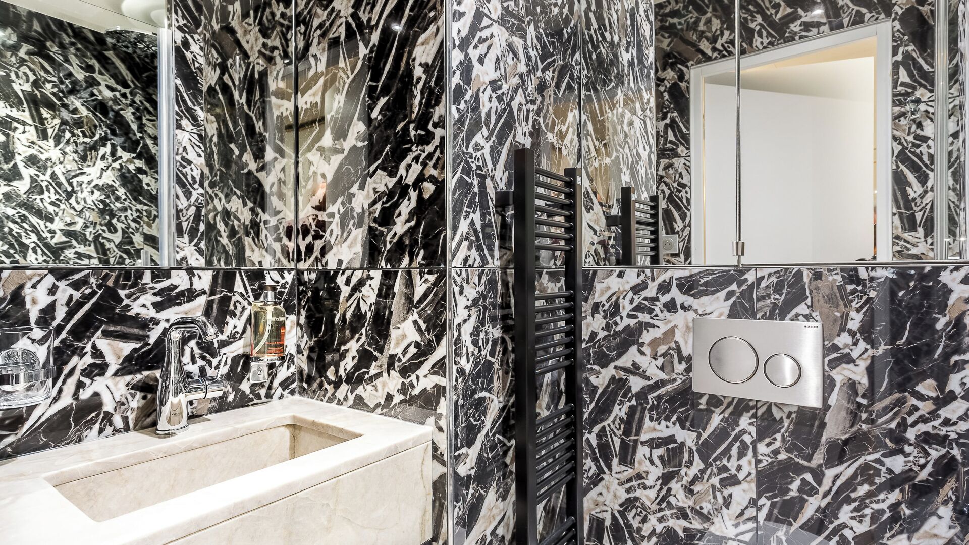 A bathroom with a sink, mirror, and black and white marble tiles.