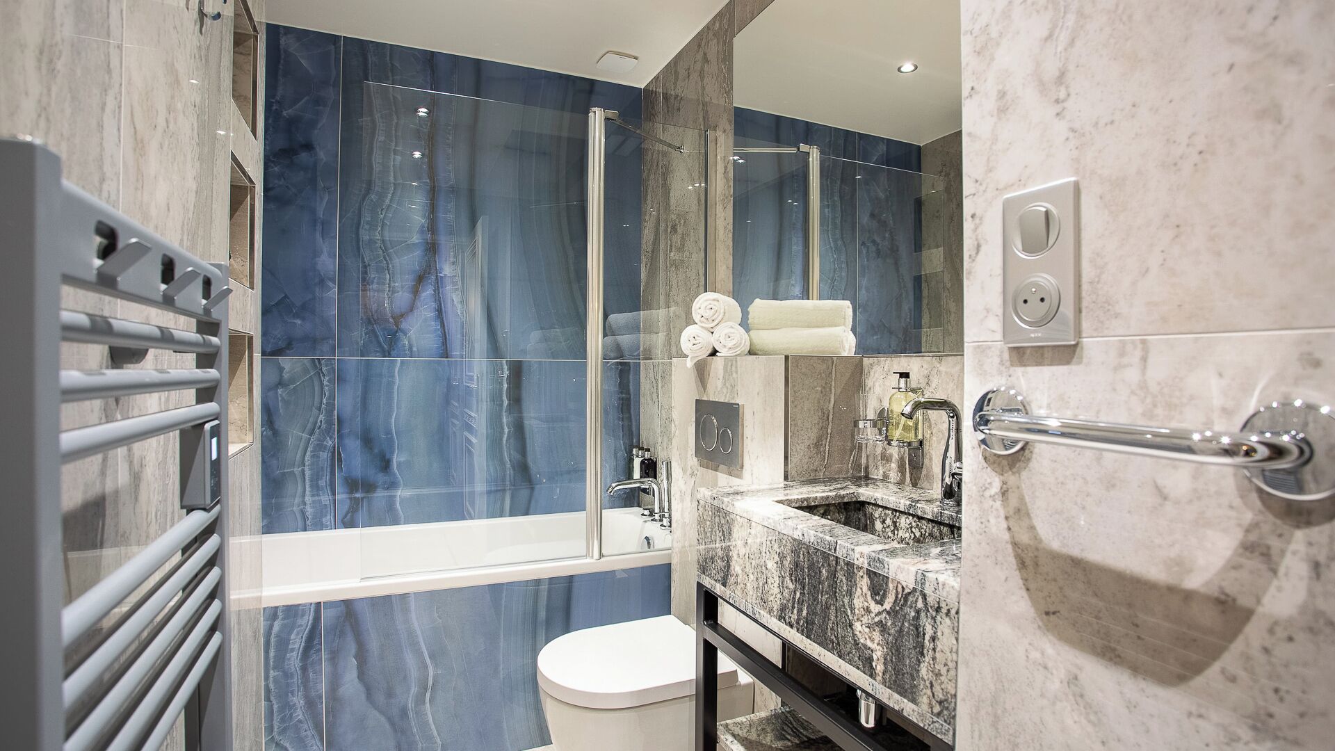 Een moderne badkamer met een douchecabine van glas, een inbouwwastafel met een marmeren blad en een toilet.