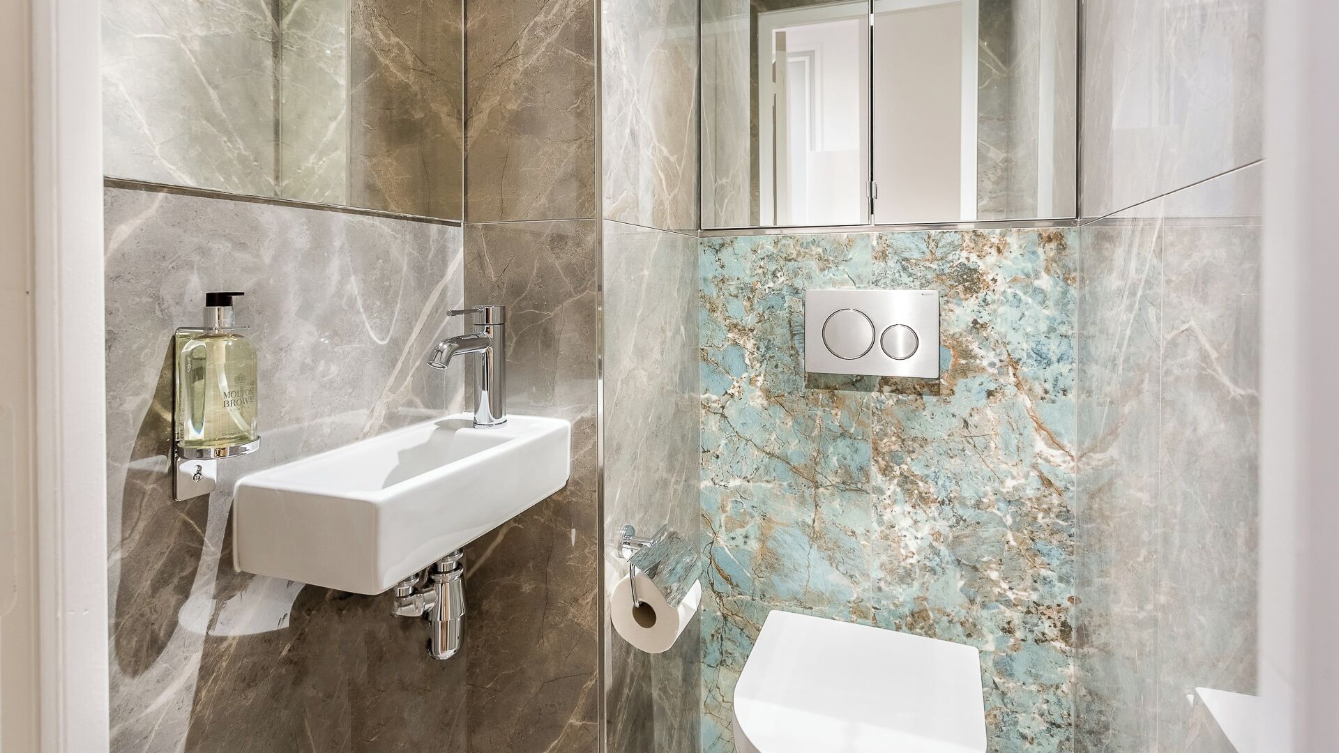 Une salle de bain avec un lavabo blanc, un miroir et un mur en marbre.
