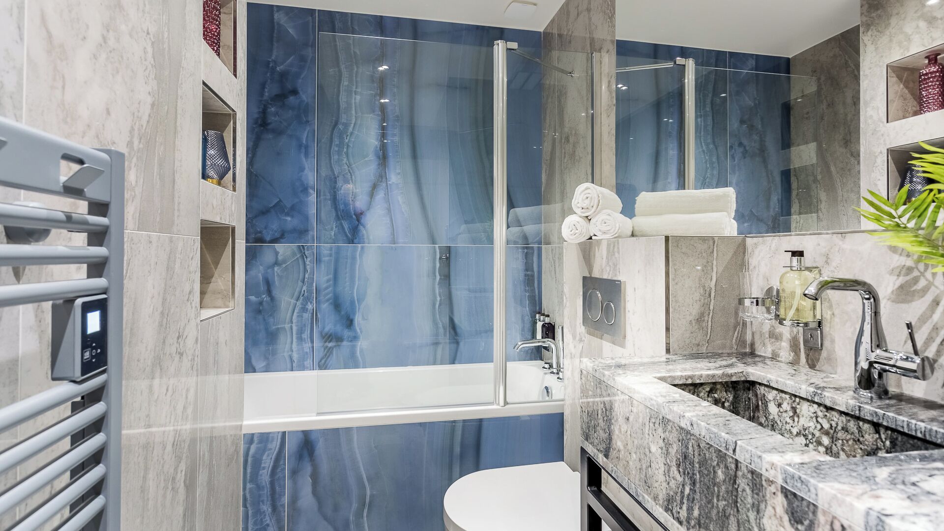 Une salle de bain moderne avec une douche à parois de verre, des carreaux de marbre, un lavabo blanc et des toilettes.