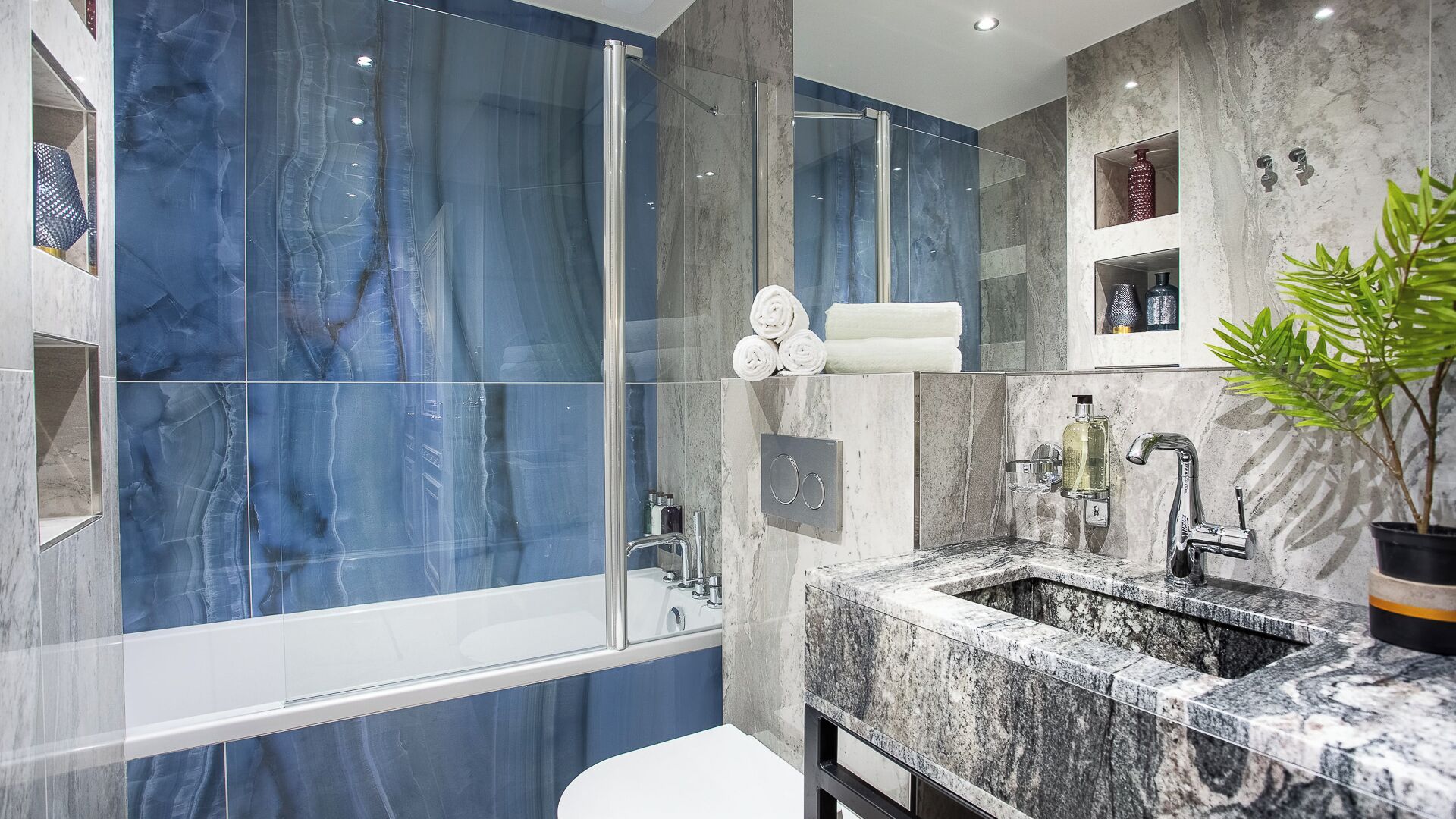 A modern bathroom with a glass shower enclosure, marble tiles, a sink with a mirror, and a potted plant.