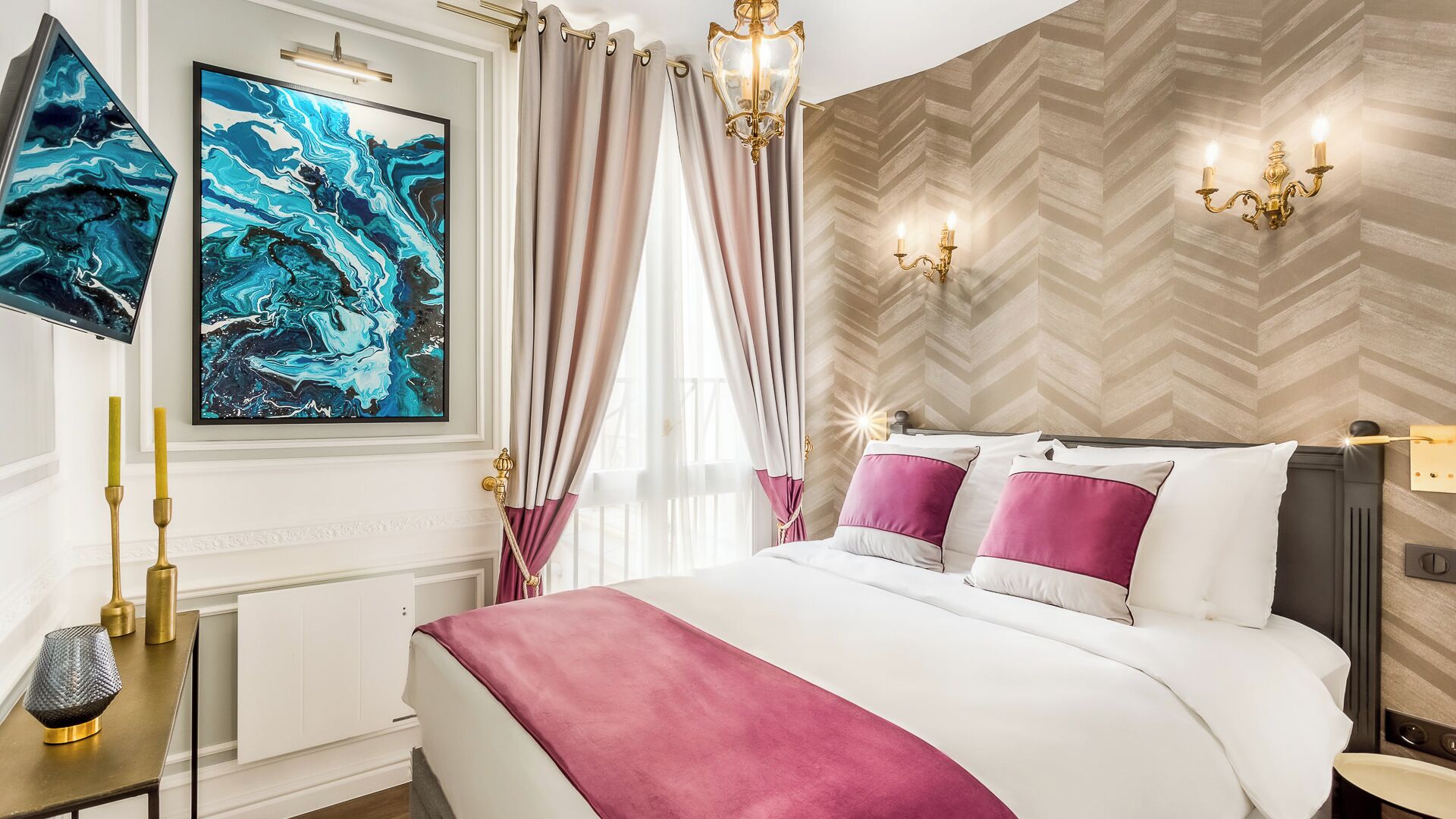 A modern bedroom with a large bed, decorative wall art, a chandelier, and a herringbone-patterned wall.