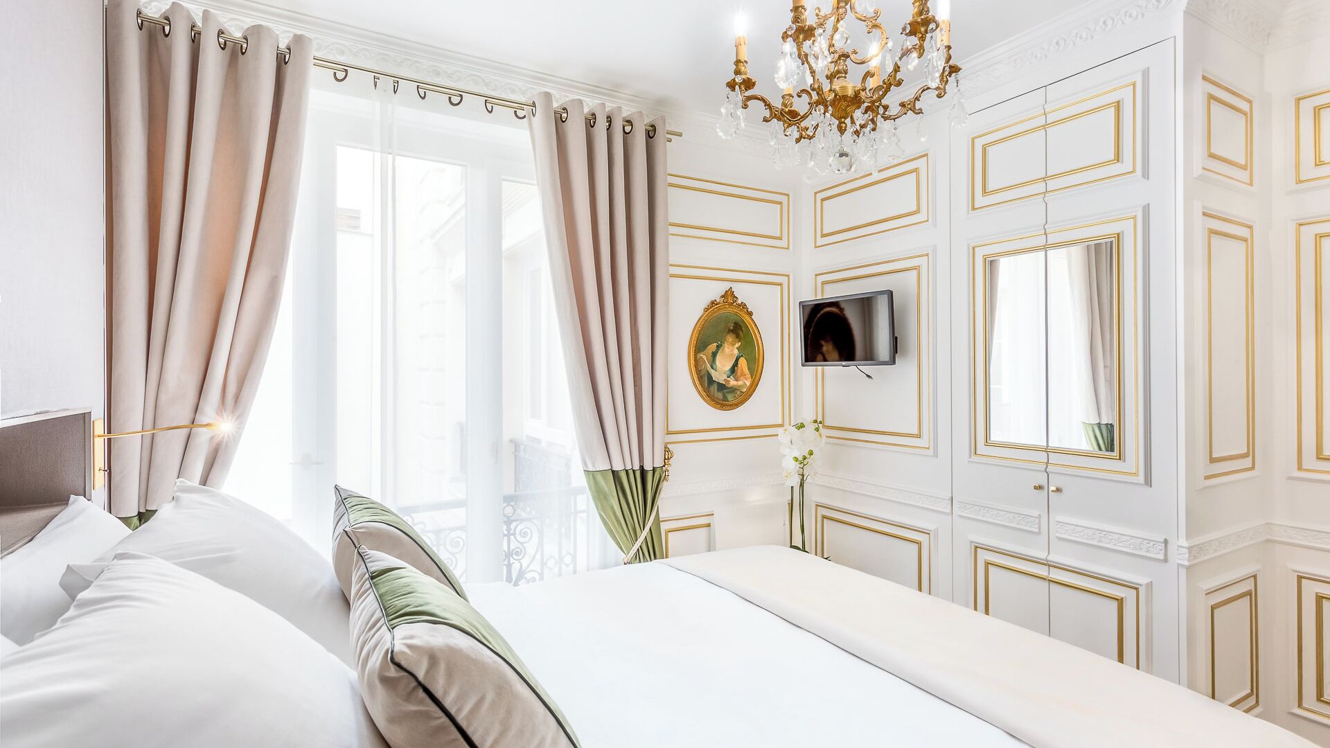 Una habitación de hotel con una cama grande, un televisor montado en la pared y un candelabro.