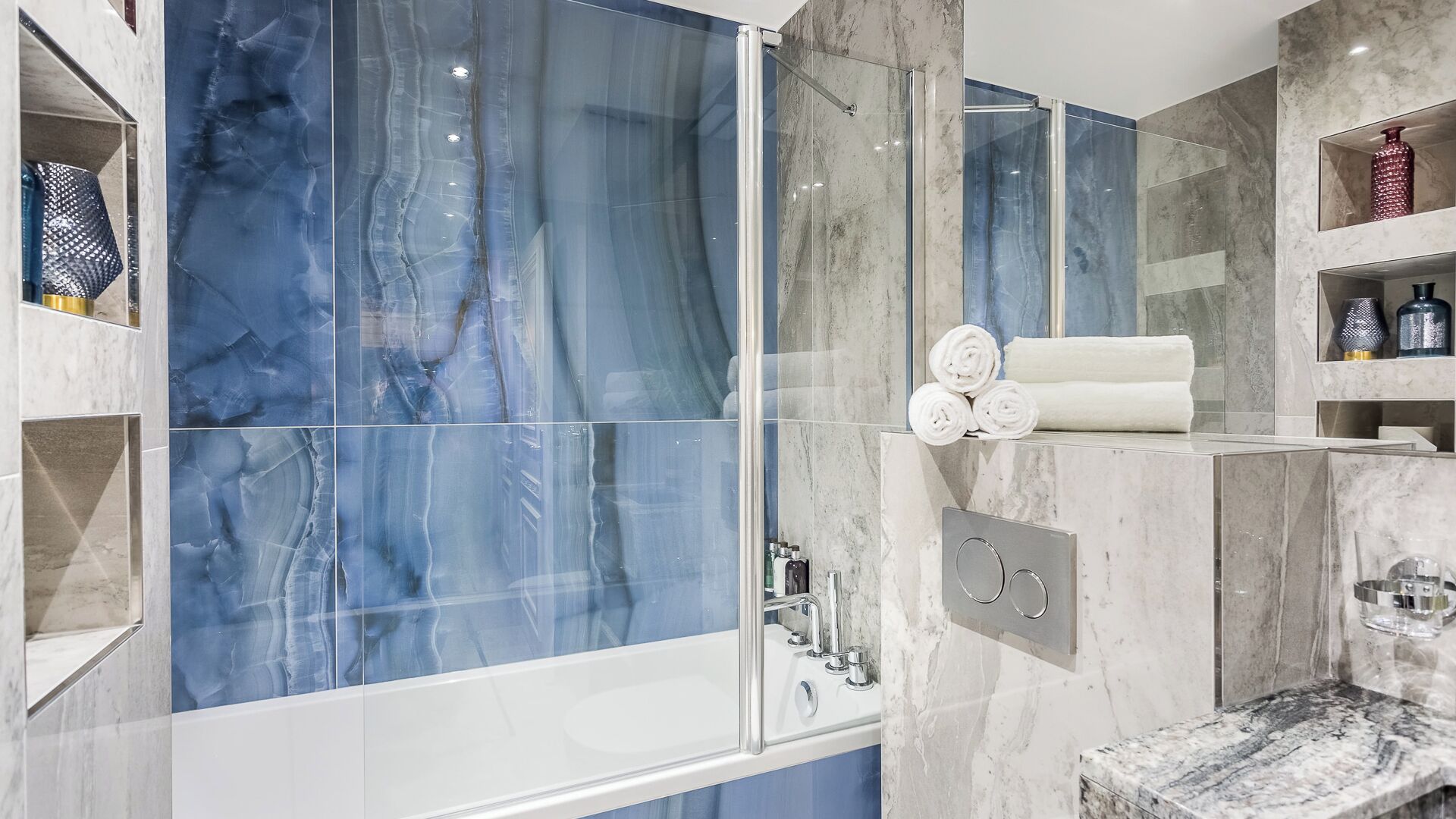 Um banheiro moderno com box de vidro, azulejos de mármore e pia embutida.