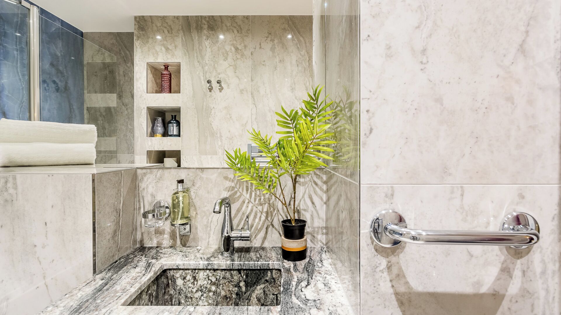 A bathroom with a marble sink, a potted plant, and a handrail.
