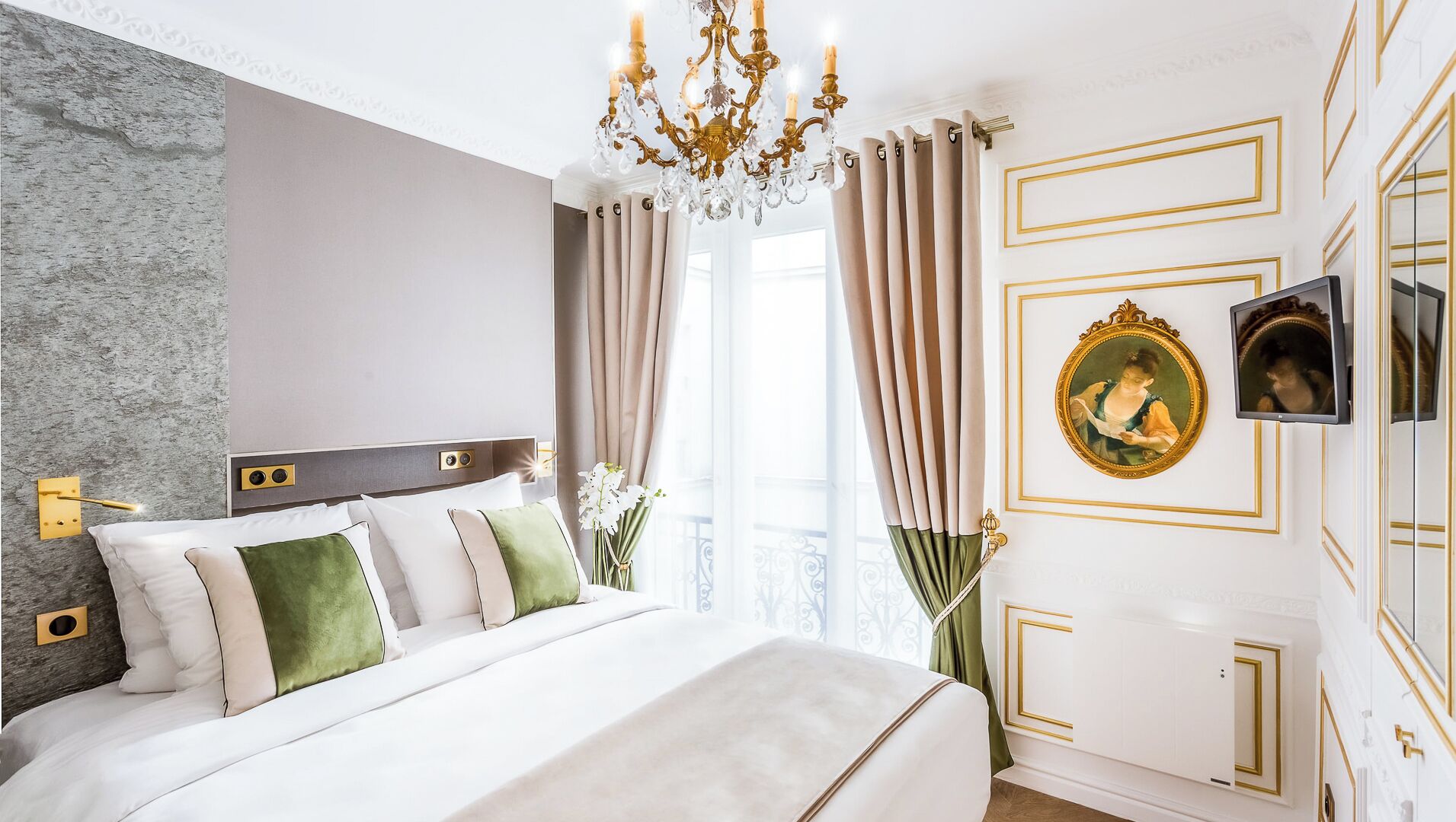 A hotel room with a large bed, a chandelier, a television, and a framed picture on the wall.