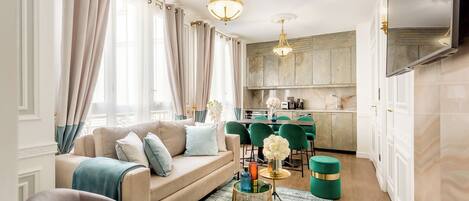 A modern living room with a sofa, green chairs, a coffee table, and a kitchen area with a dining table.