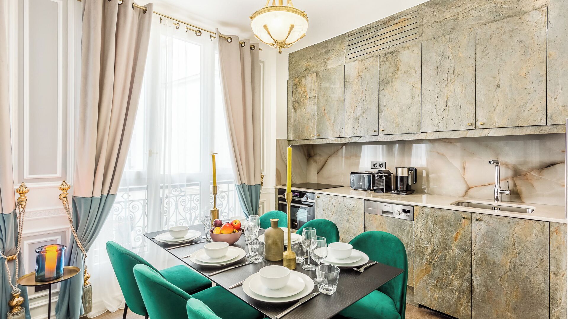 Uma área de refeições com mesa posta para quatro, uma cozinha com bancadas de mármore e uma varanda com cortinas.