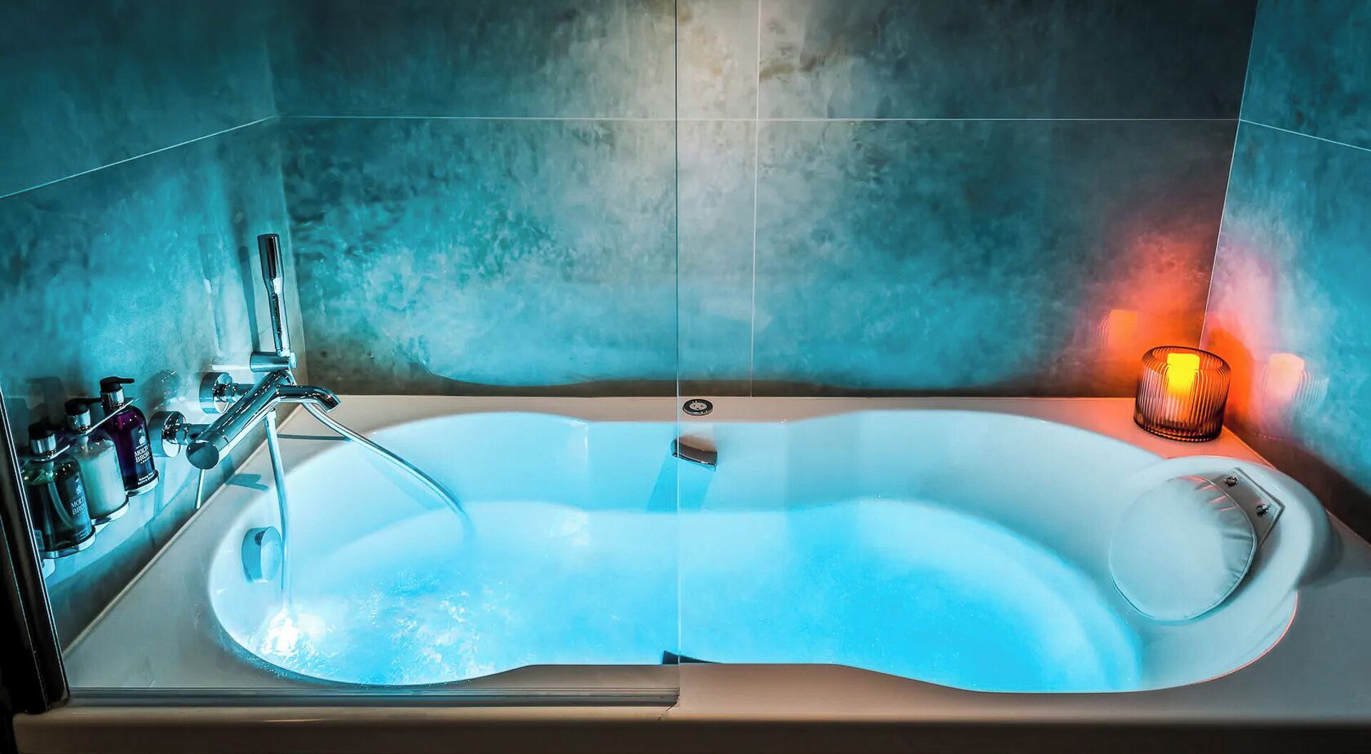 Un baño moderno con una bañera independiente, cabina de ducha con paredes de vidrio y una vela a la derecha.