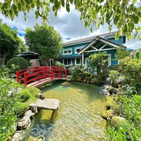 Um jardim tranquilo com lagoas límpidas, uma ponte vermelha e um edifício com telhado de azulejos.