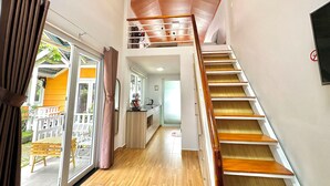 Eine Treppe führt zu einer zweiten Etage, mit einem hölzernen Geländer und Blick auf einen Balkon mit Gartenmöbeln.