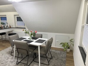 A dining area with a table and chairs, a vase with flowers, and a kitchen in the background. - Stylish Apartment for Families, Technicians, and Business Travelers in Horb (Horb am Neckar)