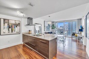 Una cocina moderna con una isla grande, un comedor con mesa redonda y vistas a un paisaje urbano a través de ventanas amplias.