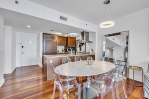 A modern kitchen with wooden cabinets, a central island, and a dining area with a marble table and clear chairs.