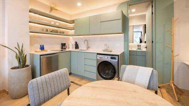 Una cocina compacta con lavadora, un comedor con mesa y sillas, y una planta en maceta.