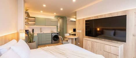 Una habitación de hotel moderna con una cama grande, un televisor montado en la pared, una kitchenette y un baño pequeño.