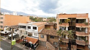 Un edificio de varios pisos con fachada de ladrillo, balcones con plantas y vista a la calle con tiendas y un restaurante.