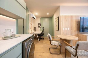 Cocina compacta con lavavajillas, cafetera y zona de comedor con mesa redonda y dos sillas.