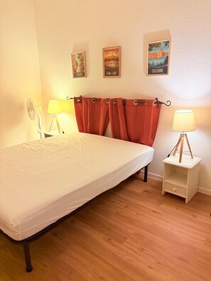 Un dormitorio con una cama, dos lámparas de noche, una mesita auxiliar pequeña, un ventilador y tres cuadros colgados en la pared.