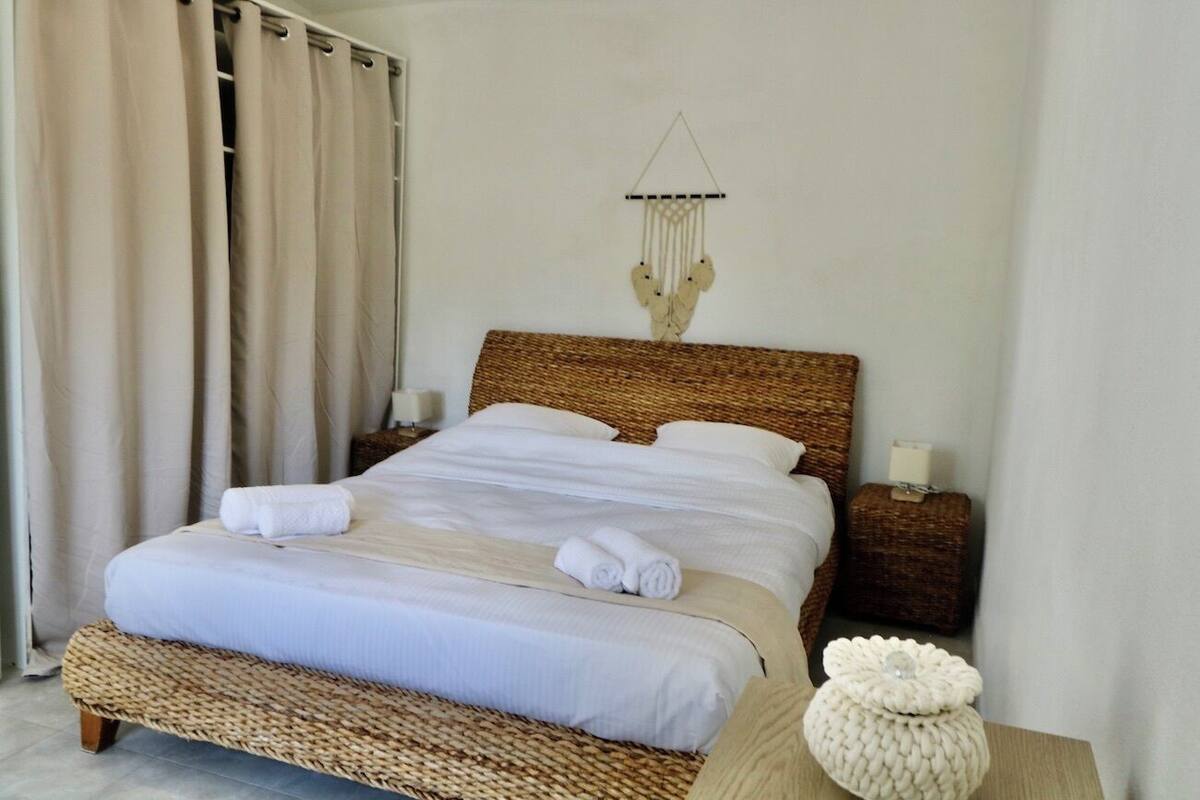 A neatly made bed with white linens and a woven headboard, a bedside lamp, and a decorative wall hanging.