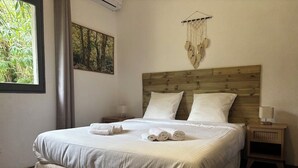 A neatly made bed with white linens and rolled towels, a wooden headboard, a wall-mounted macrame piece, and a small bedside table with a lamp. - GÎTES TERRA DI A BRAVONA (Linguizzetta)