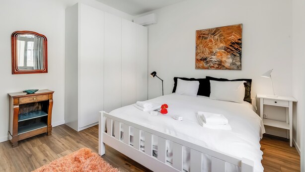 Una camera da letto moderna con un letto bianco, un comodino di legno, uno specchio e un quadro appeso al muro.