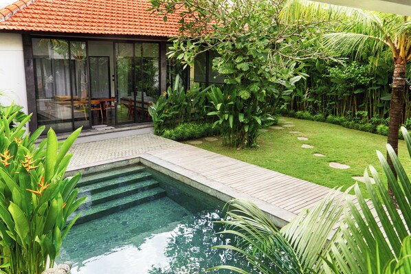 A modern house with a swimming pool, wooden deck, and lush garden.