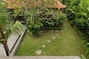 A garden with a paved walkway, lush greenery, and a building with a red roof.