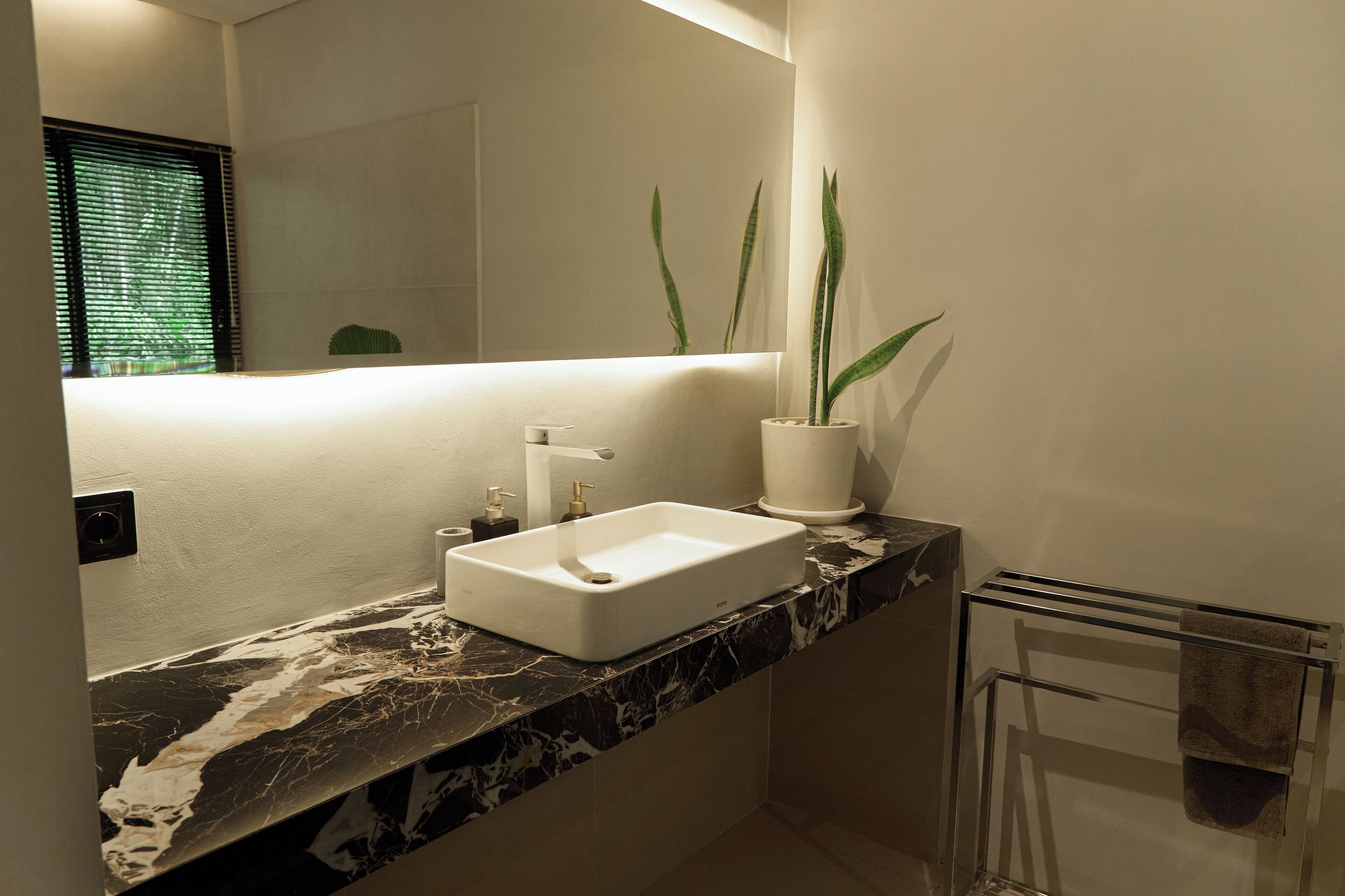 Une salle de bain avec un lavabo blanc, un miroir et une plante en pot.