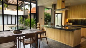A modern kitchen with a large island, wooden cabinets, and a view of a pool and greenery outside.