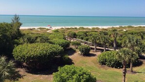 Vista costera con playa, un puente de madera y vegetación densa.