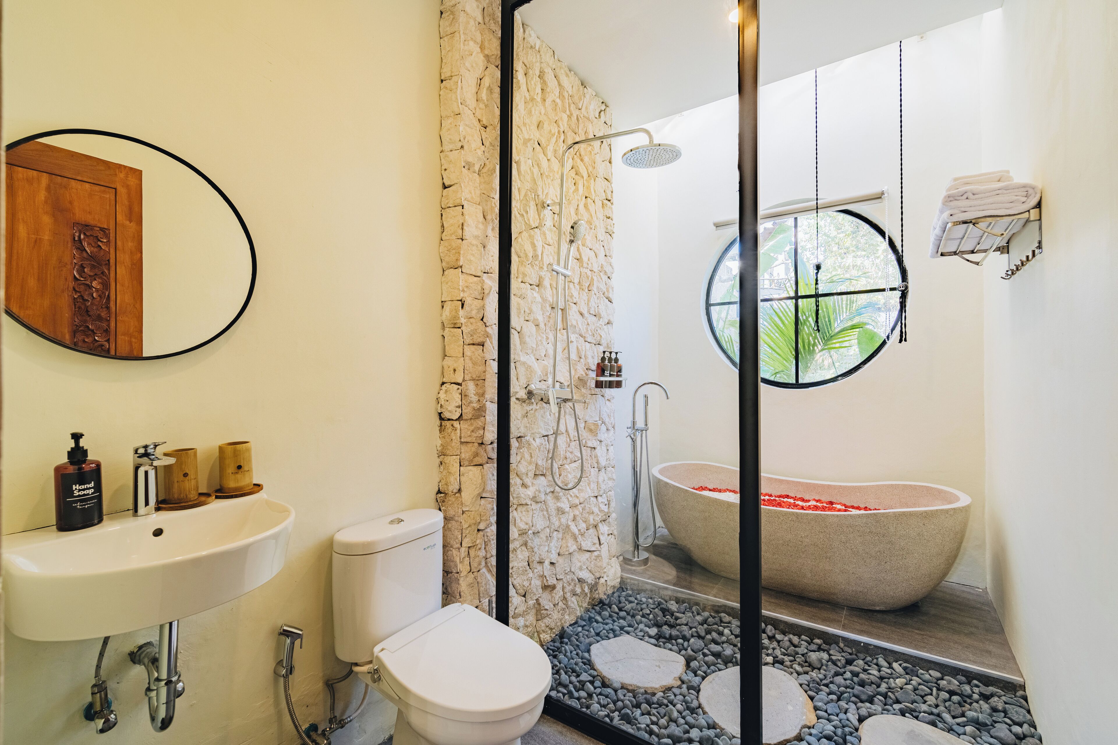A bathroom with a stone wall, a freestanding bathtub, a sink, and a toilet.