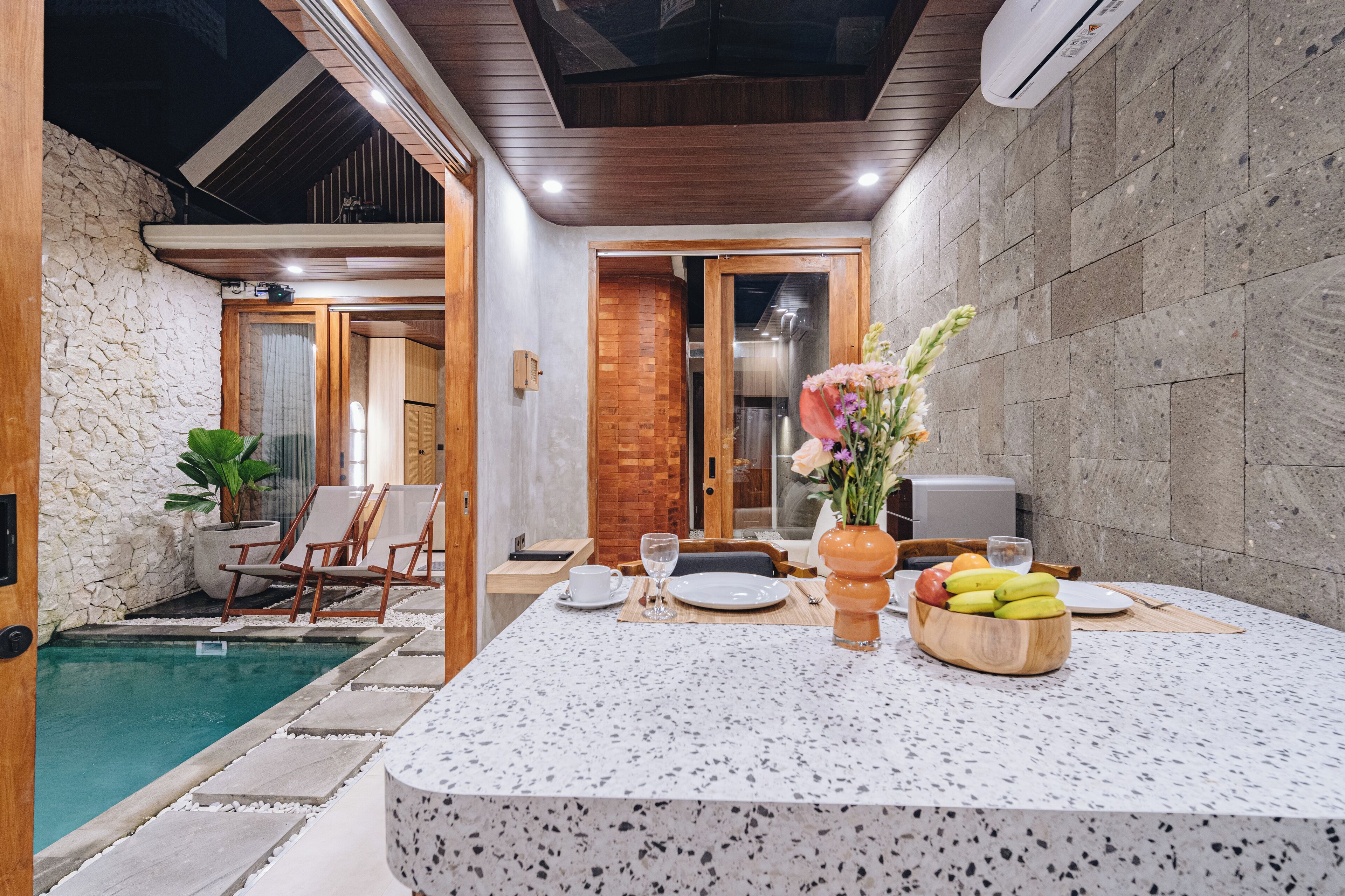 A modern dining area with a pool, stone walls, and a wooden ceiling.