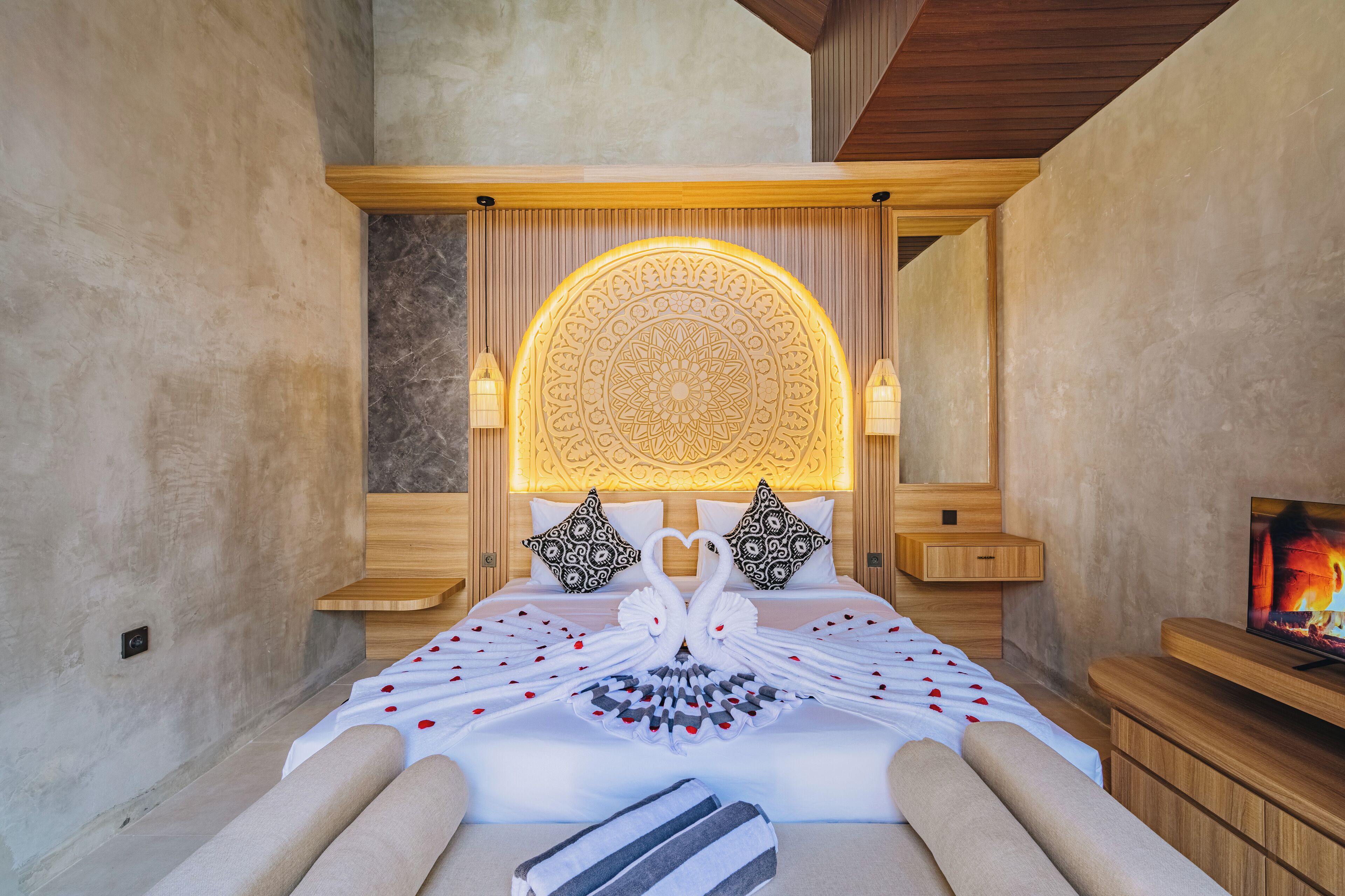 A hotel room with a large bed, a decorative wall panel, two wall-mounted lamps, and a television on a wooden stand.