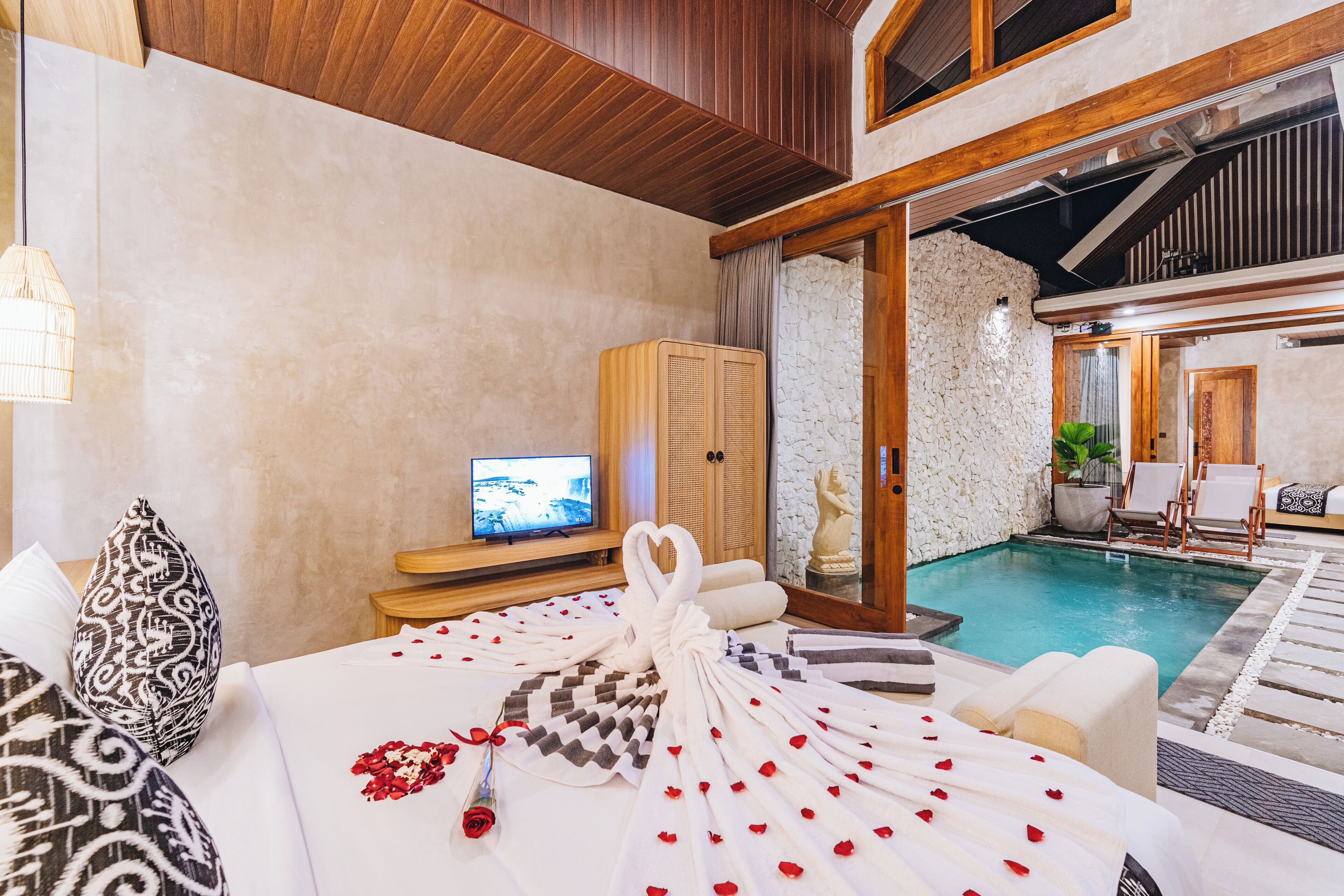 Camera d'albergo con un letto, una televisione, un muro in pietra, una piscina e vista sulla zona della piscina.