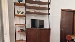 Ett vardagsrum med en soffa, en tv-apparat på ett träbord, ett matbord och stolar.