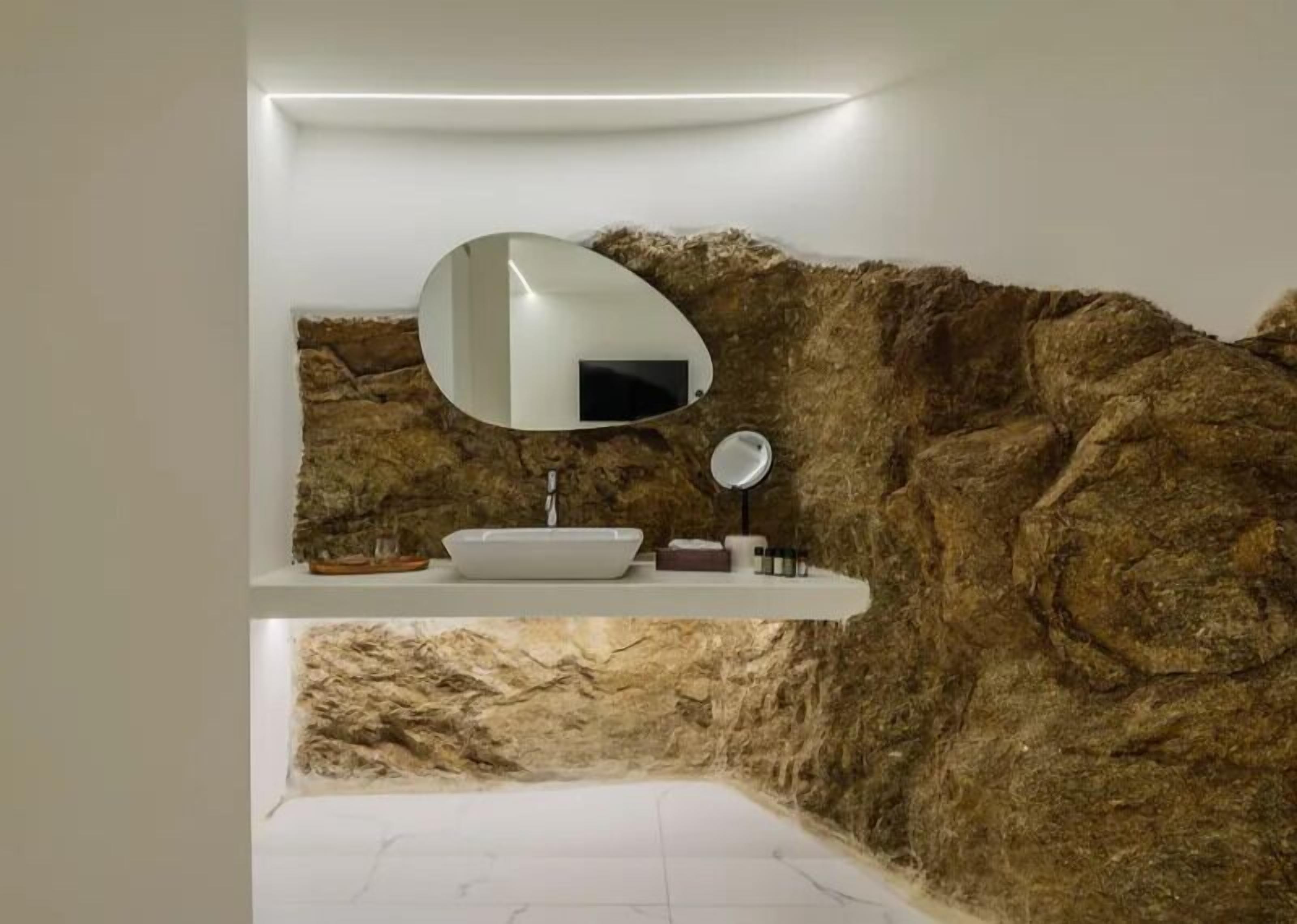 Un baño con un lavamanos blanco, un espejo redondo y un estante con artículos de aseo.