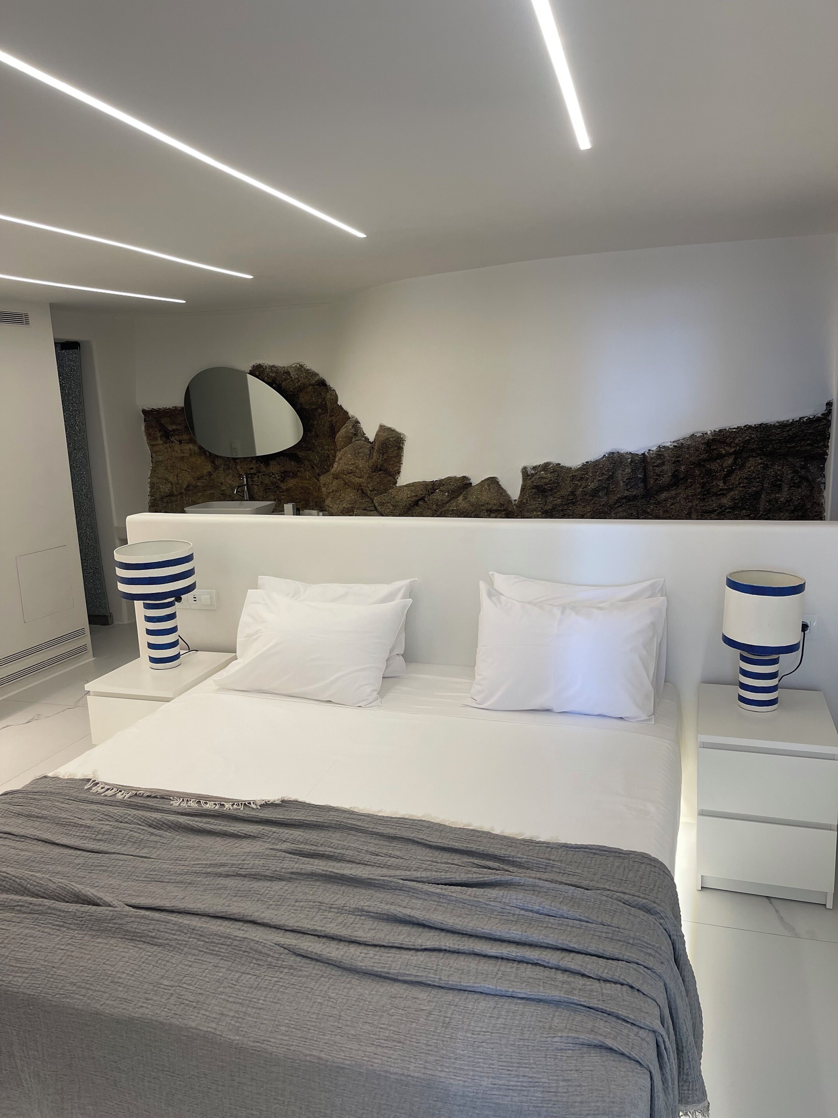 A modern bedroom with a large bed, white bedding, and two bedside tables with lamps.