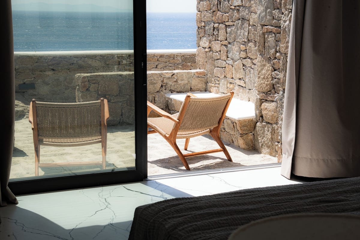 Una habitación con vista al mar a través de un ventanal, que incluye una silla de mimbre y una mesita.