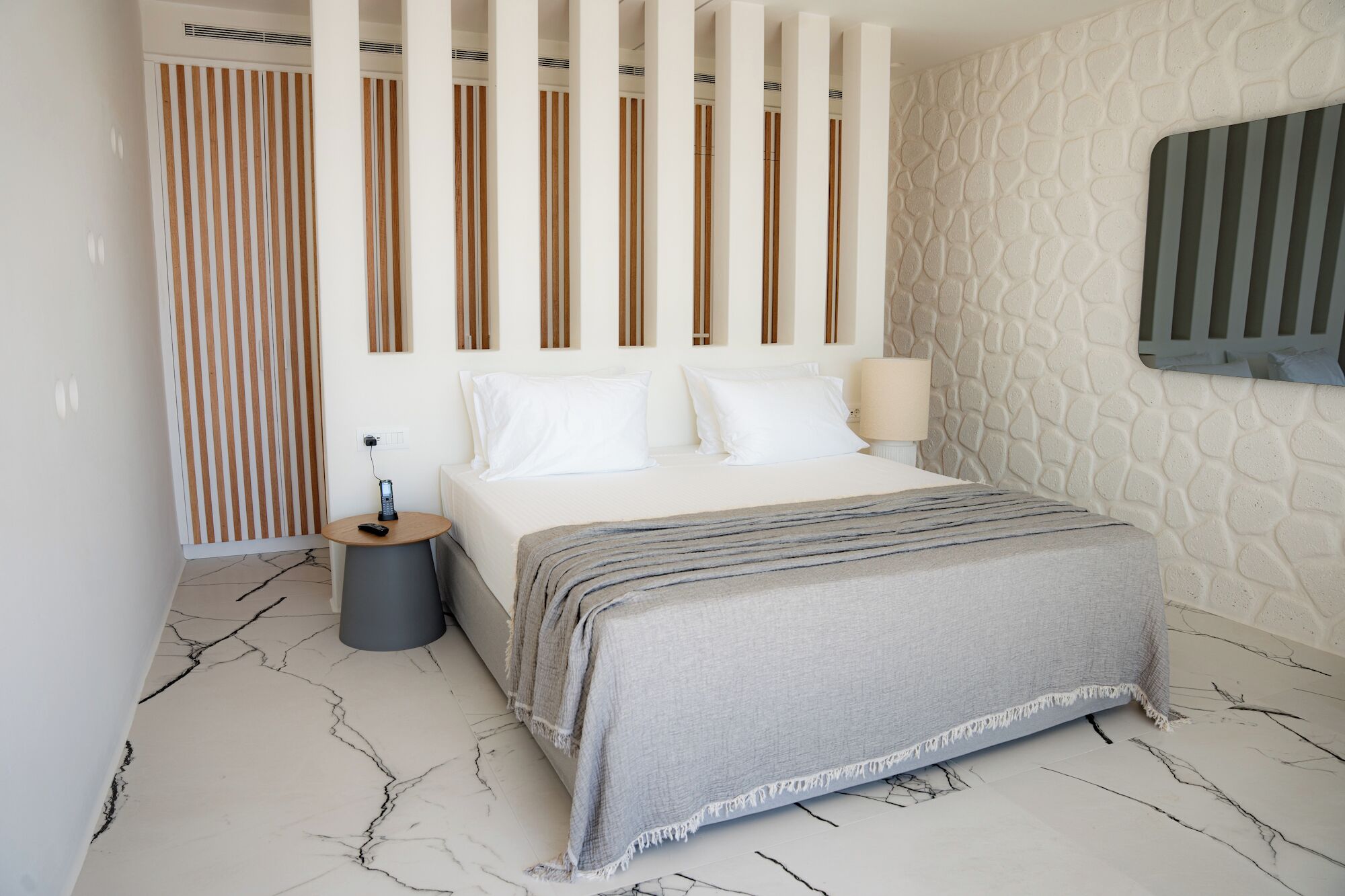 A modern bedroom with a bed, bedside table, lamp, and a unique textured wall.