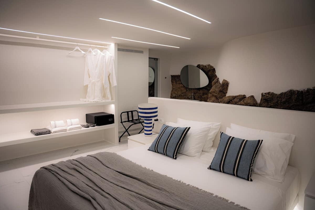 Un dormitorio moderno con una cama grande, mesitas de noche, un espejo y un estante en la pared con toallas.