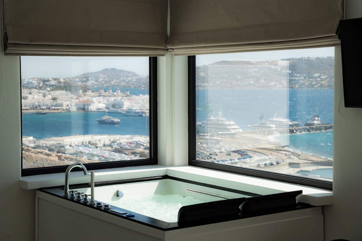 Un baño moderno con bañera, una ventana con vistas a un pueblo costero y un puerto deportivo.