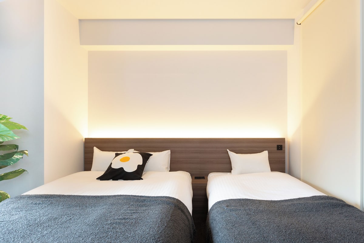Quarto de hotel com duas camas de solteiro, cabeceira de madeira, roupa de cama branca e uma janela grande.