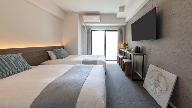 A modern hotel room with two beds, a flat-screen TV mounted on the wall, and a large window providing a view of the outdoors.