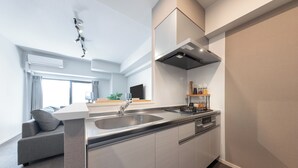 A modern kitchen with a built-in sink, stainless steel appliances, and a grey sofa in the adjacent living area.