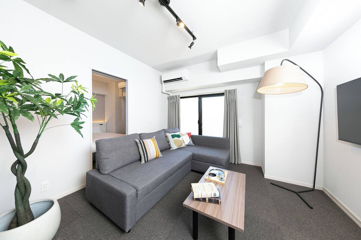 Uma sala de estar moderna com um sofá modular cinza, uma mesa de centro, um abajur e um vaso de planta.