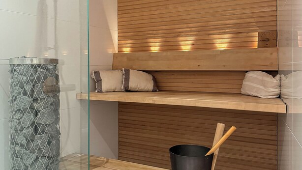 A modern bathroom with a glass shower enclosure, wooden shelves, and a black basin with a wooden spoon.